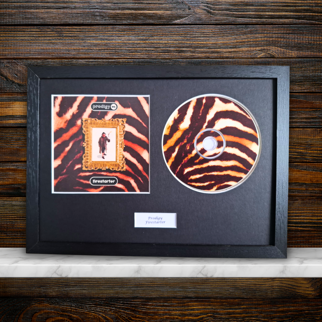 A framed custom CD album display featuring a zebra-print CD with a custom album cover insert, mounted in a black frame on a marble shelf against a dark wood background.