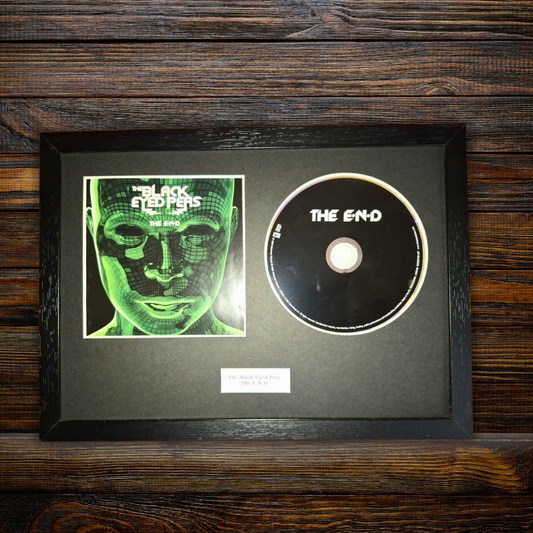 A framed black CD album for 'The Black Sheep' by 'The End' is displayed on a dark wood background. The frame contains the CD disc alongside a green-tinted square cover print of a face in a grid pattern, with a small white label at the bottom.