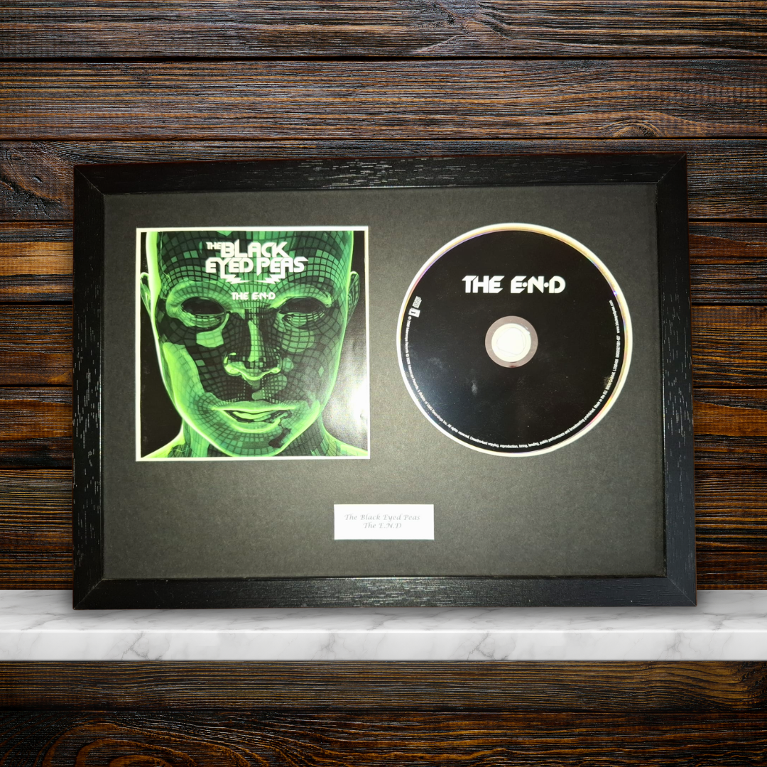 A framed black album print and CD set for the band 'The Blackened', featuring a green-toned square album cover and a black CD with white text, mounted in a black frame against a dark wood background.