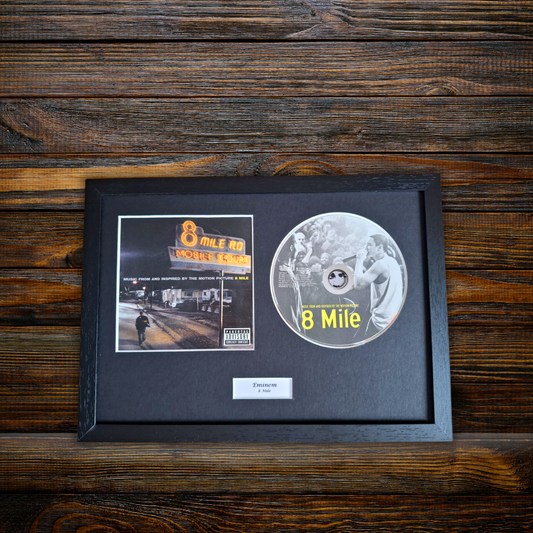 A framed 8 Mile music memorabilia piece featuring the album cover art, a silver CD, and a small plaque, displayed on a dark wood background.