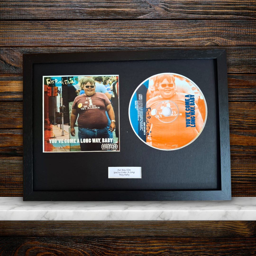 A framed custom album memorabilia piece featuring a printed photo of a man and a custom vinyl record on a black mat, displayed on a white marble surface against a dark wood background.