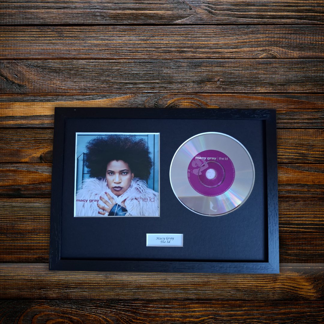 A framed music memorabilia piece featuring a small portrait photo of Midge Harper and a silver CD with a purple center label, mounted in a black frame on a dark wood background.