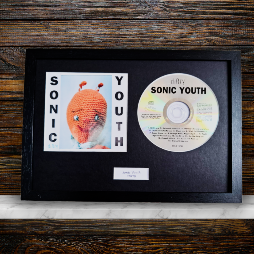 A framed Sonic Youth memorabilia piece featuring the band's 'YOUTH' album cover, a CD, and a small plaque inside a black frame, displayed on a marble surface against a dark wood background.