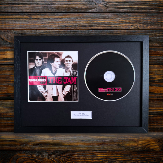 A framed and mounted Sound of The Jam CD single, featuring the black CD disc, a printed album cover insert, and a small white label plaque inside a black frame, displayed on a dark wood background.