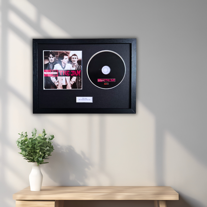 A framed The Star album display hanging on a light gray wall above a wooden console table with a small green plant in a white vase. The display includes a black frame with a printed album cover and a black vinyl record.
