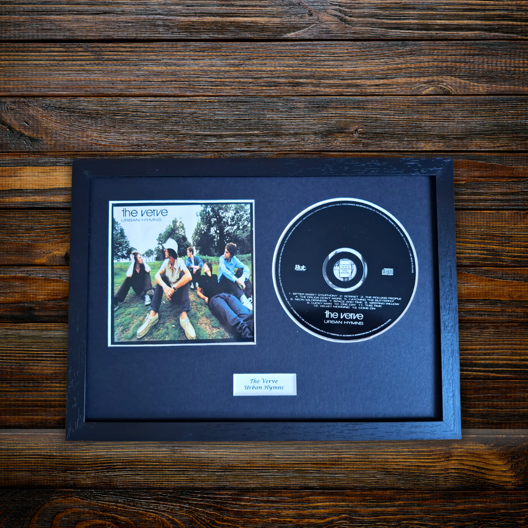 A framed CD single display featuring the band The Veetie, with a printed album cover photo and a black CD inside a dark wooden frame, placed on a dark wood surface.