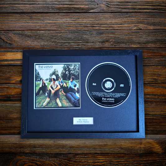 A framed CD single display featuring the band The Veetie, with a printed album cover photo and a black CD inside a dark wooden frame, placed on a dark wood surface.
