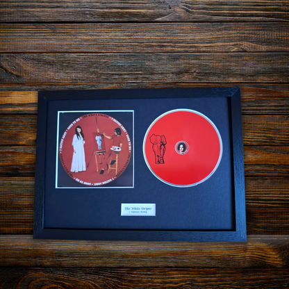 A framed CD set on a dark wood background. The black frame contains a red vinyl disc with an elephant illustration and a printed album cover insert for 'The White Stripes'
